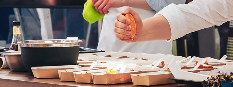 A chef squeezing an orange over cartons of food during a cooking demonstration